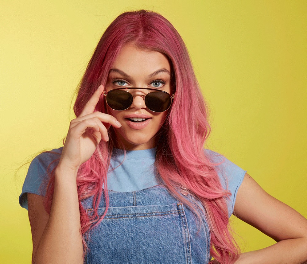 young model with pink dyed hair peering over sunglasses