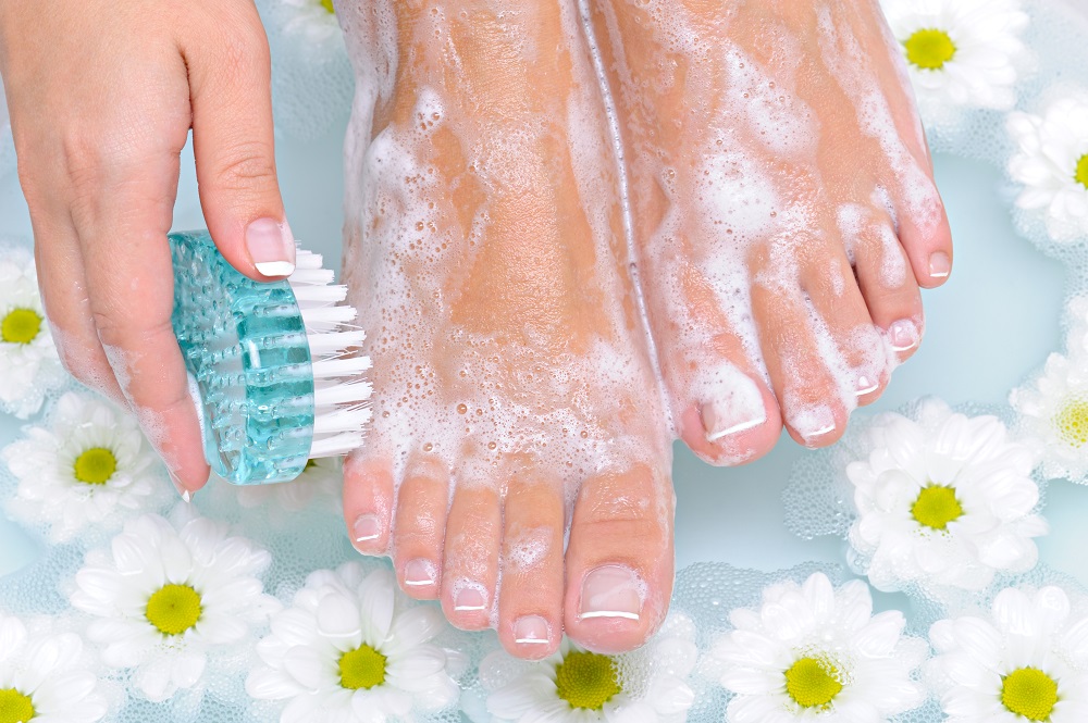 The young woman washes and cleans the beautiful well-groomed legs in water by means of a clearing brush