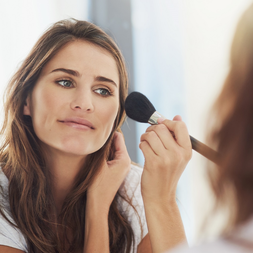 female applying bronzer looking in the mirror