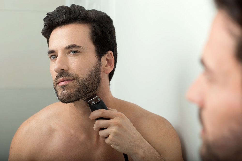 Mens Beard Guide-life-style-model-looking-into-mirror-grooming-beard-electric-razor-in-bathroom