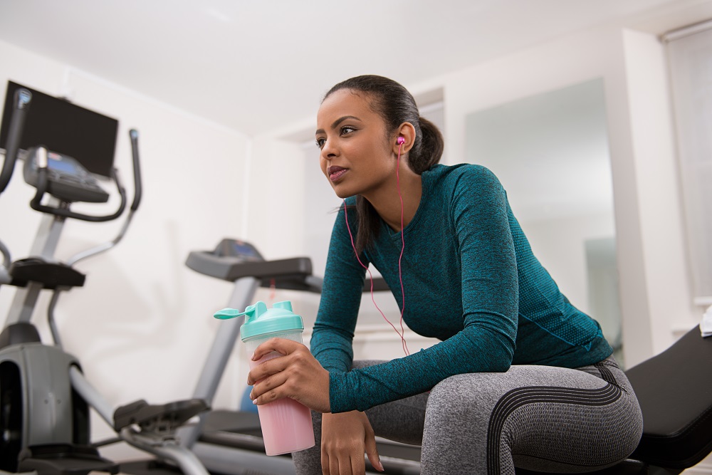 Girl in gym listening to music holding a strawberry protein shake