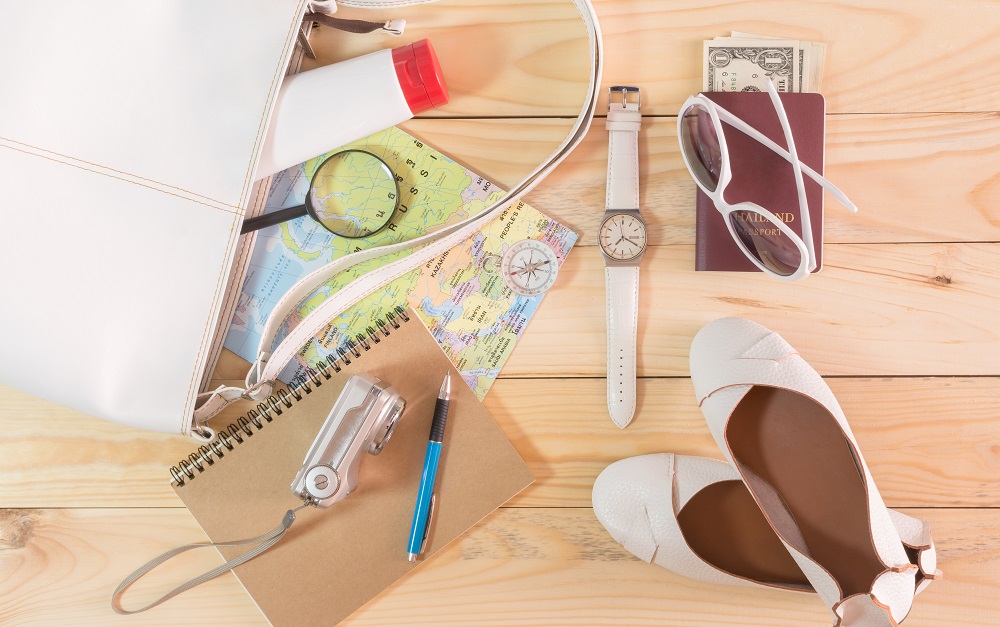 Travel concept with leather handbag, sunglasses, digital camera, world map, passport, money, note pad, pen, magnifying glass, compass, female shoes, body lotion and wristwatch on wooden table