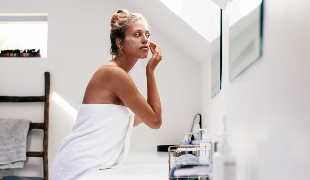 woman looking in the mirror and applying cream to her face