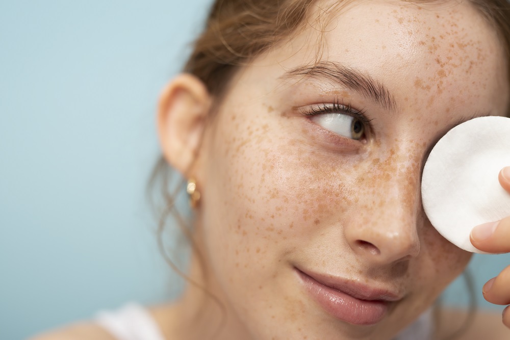 Young, fiar skinned laduy removing eye makeup with a cotton pad