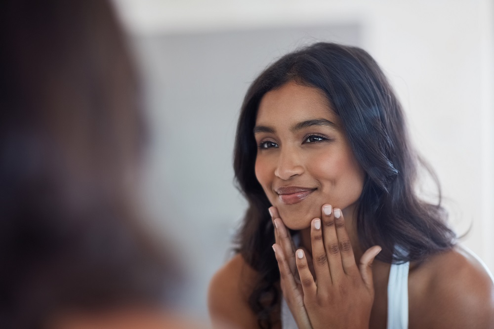 Young woman with clear skin touching face after applying glycolic acid