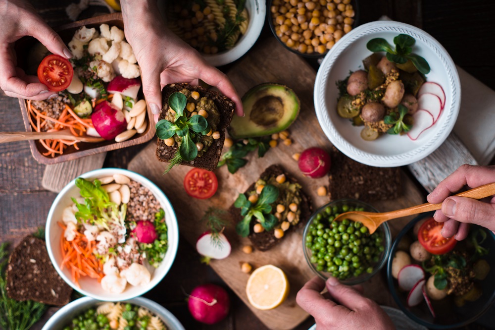 Vegan dishes displayed on a table with hands reaching for food