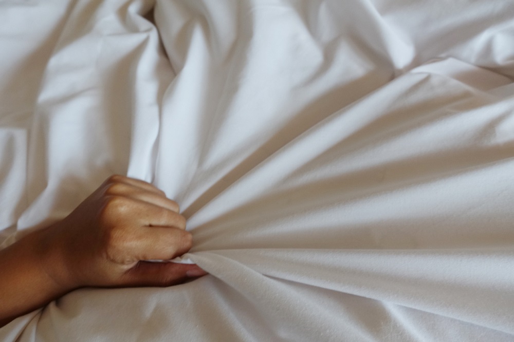 Woman's hand clutching at bed sheets