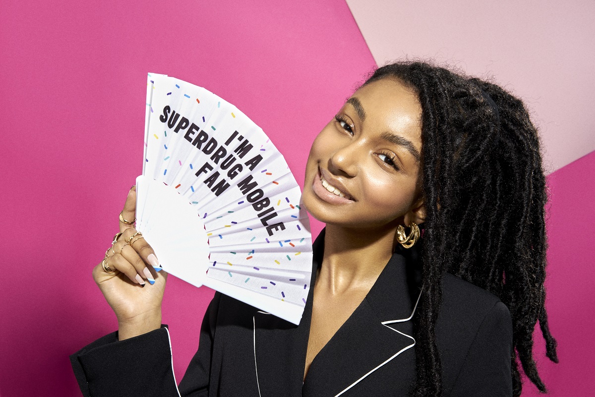 Young female holding a Superdrug Mobile fan in front of a pink background