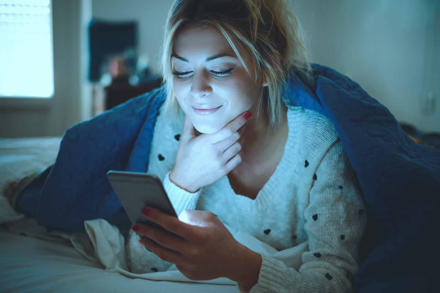 Portrait of a cheerful young girl texting and lying on the bed