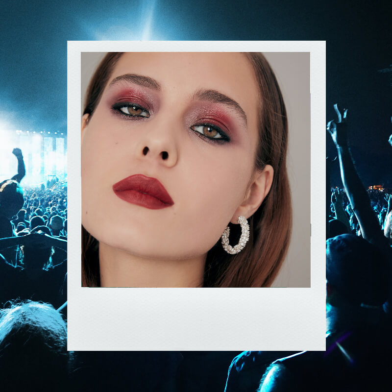 Festival beauty in the 80s with dark haired female wearing grungy eye makeup and a dark red lip. 