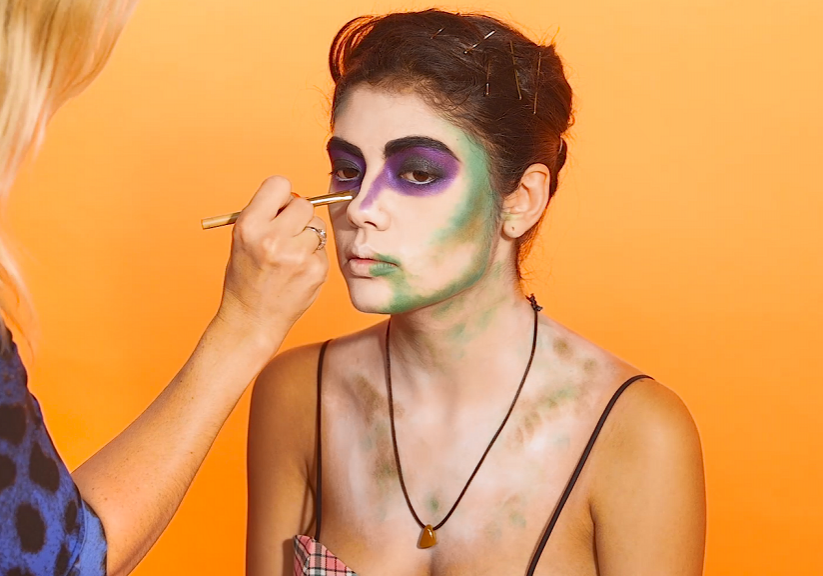 MUA adding green face paint to model's face to create a Beetlejuice makeup look