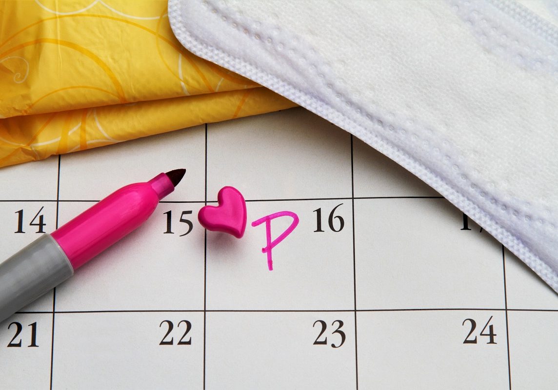 Calendar with date marked with heart push pin and letter P. Menstruation concept. Women's personal hygiene items: pads and liners.   Creative content brief 683313911.