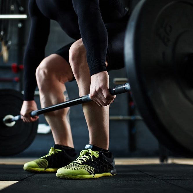 Active young man training with barbell in gym